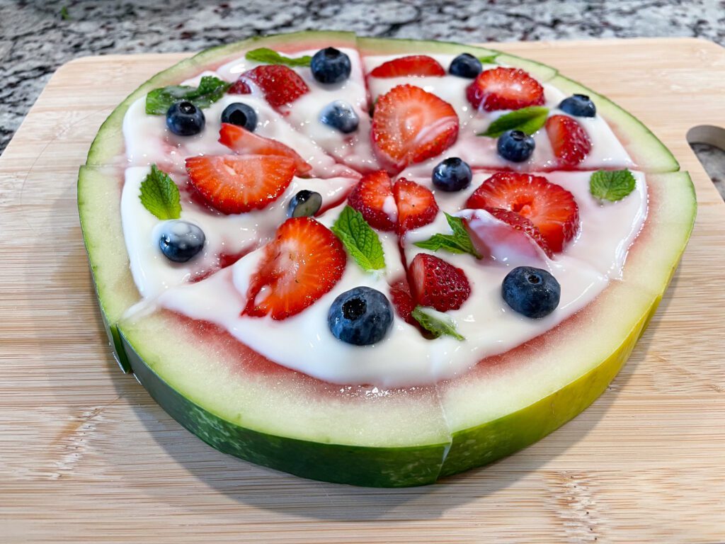 Watermelon with yogurt, berries, and mint on top, sliced into pizza slices.