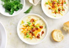 Creamy potato soup with bacon and cheddar cheese in bowl on light stone background. Healthy diet dish for dinner. Top view, flat lay