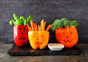 Healthy Halloween food. Vegetables and dip in Jack o Lantern bell peppers. Side view against a dark background.